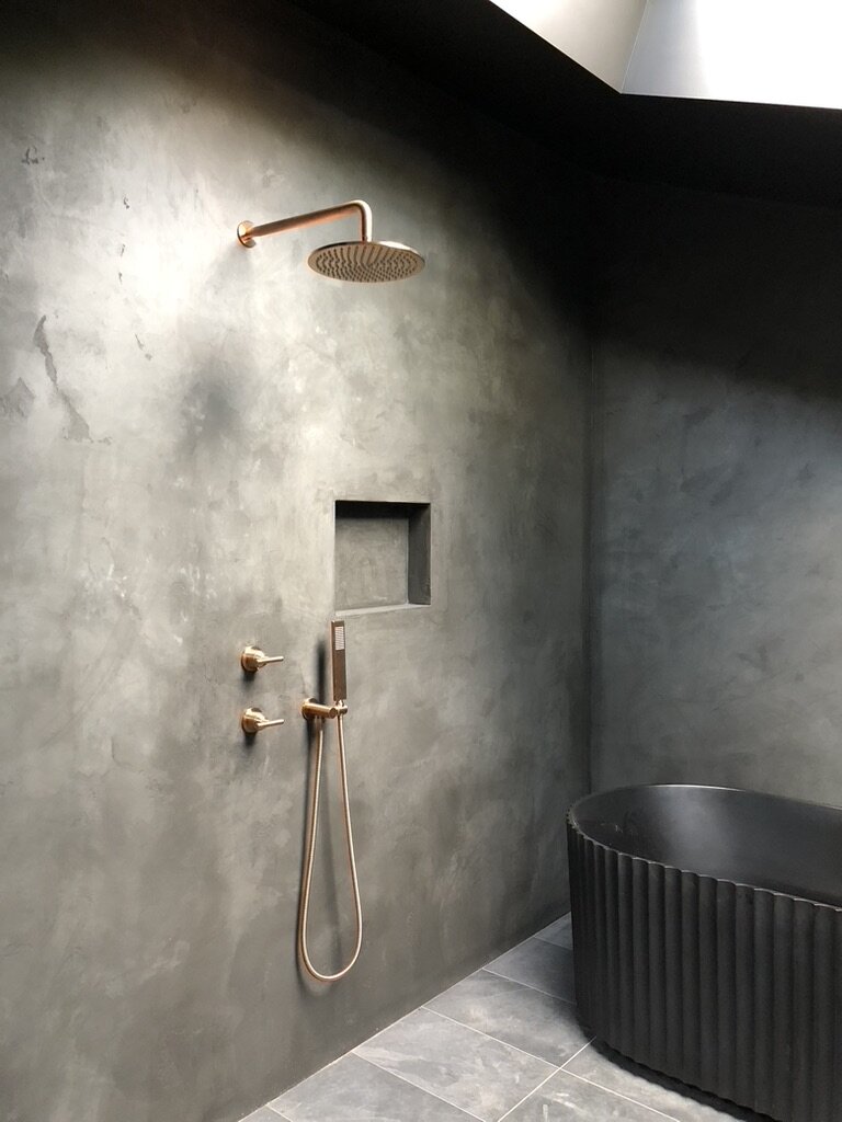 Modern architect designed bathroom with dark microcement rendered walls, copper finish fittings and black scalloped free-standing bath